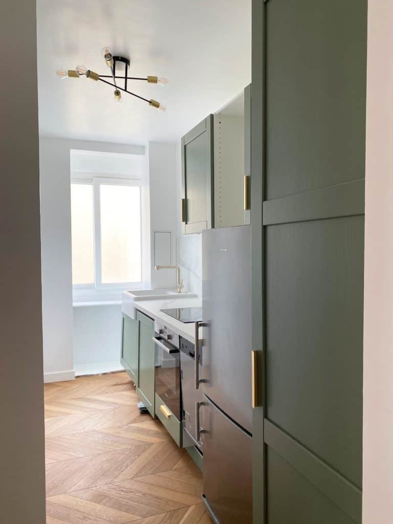 Cuisine rénovée parquet chevron meubles verts plafonnier doré et noir