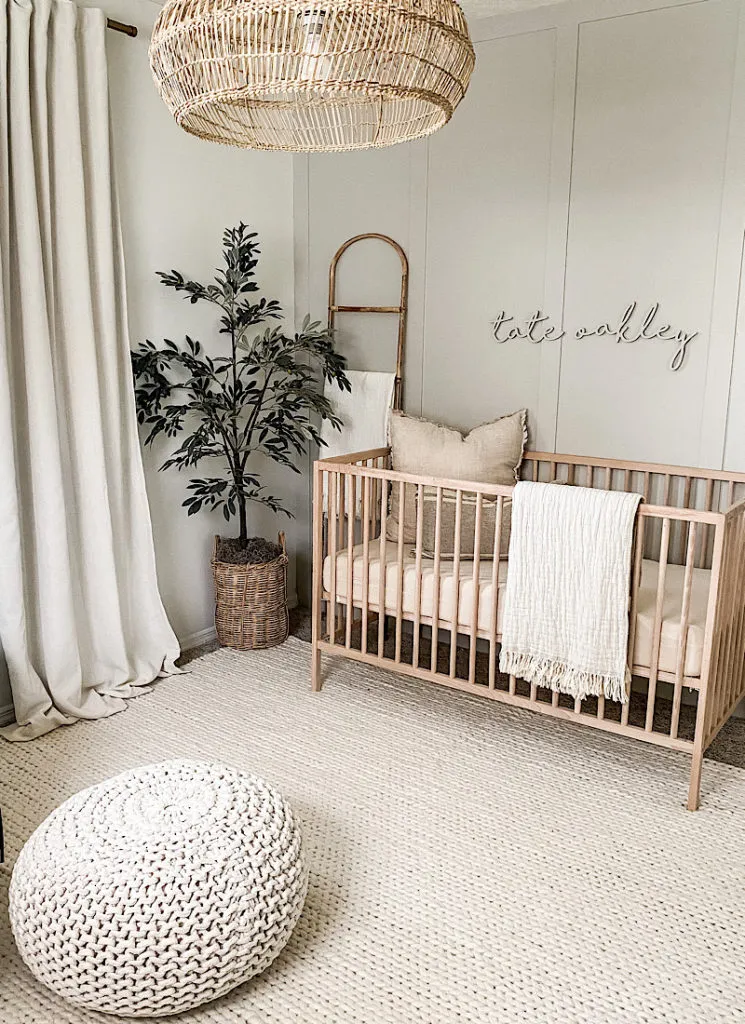 Chambre bébé naturelle avec lit à barreaux en bois clair, suspension en rotin, tapis clair et décoration aux matières naturelles.